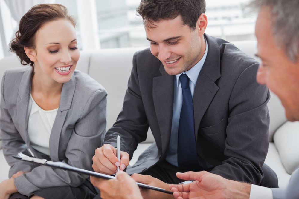 Businessman signing contract while his partner is looking at him in cosy meeting room Businessman signing contract while his partner is looking at him in cosy meeting room